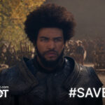 A serious-looking man in dark medieval armor stands between two wooden beams, staring ahead with determination. He has a full beard and a large afro hairstyle, with glowing golden eyes. Behind him, a crowd of people and wooden structures are visible under autumnal trees. Overlay text reads “SaveWOT” and “#SAVEWOT,” with the URL “savewot.com.”