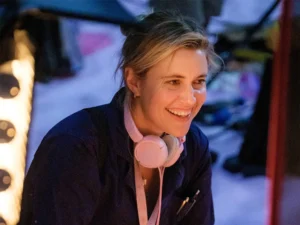 Greta Gerwig wearing pink over-ear headphones around her neck