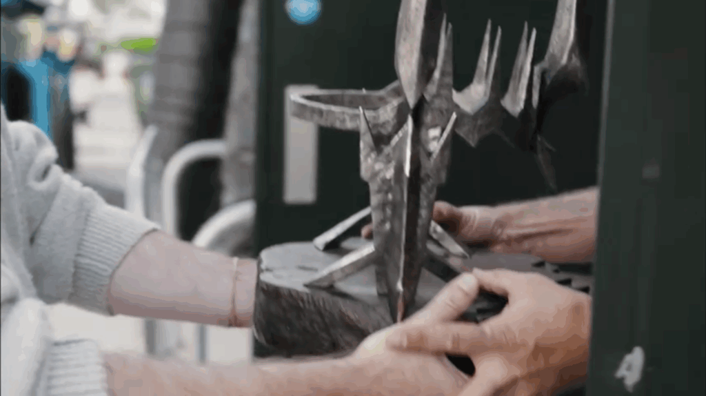 A spiky metal crown being handed from one person to another. We only see a close-up of their hands.