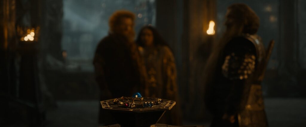 The Seven Dwarven rings sitting in their holder on the table while Durin IV, Disa and Narvi discuss in the background