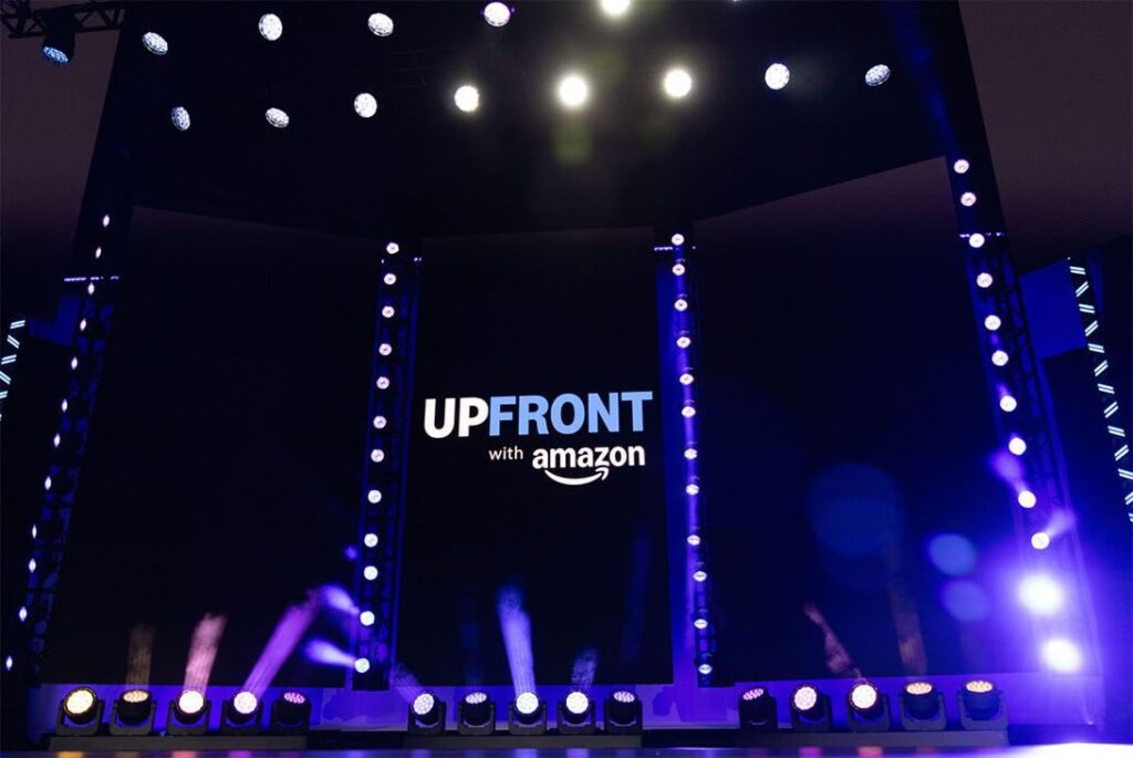 Black "Upfront with Amazon" poster lit with moody purple up-lights