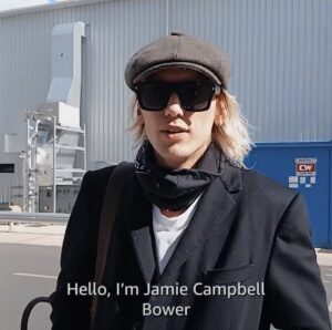 Photo of Jamie Campbell Bower in everyday clothes in front of a studio building, with subtitle "Hello, I'm Jamie Campbell Bower"