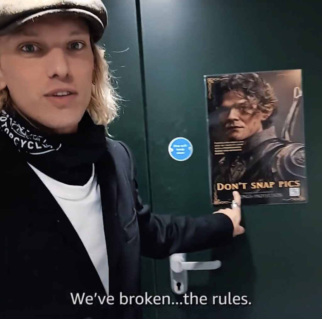 Photo of Jamie Campbell Bower in everyday clothes in front of a studio door with a photo of Elrond with label "Don't snap picts". Campbell Bower is captioned as saying "We've broken ... the rules"
