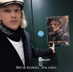 Photo of Jamie Campbell Bower in everyday clothes in front of a studio door with a photo of Elrond with label "Don't snap picts". Campbell Bower is captioned as saying "We've broken ... the rules"