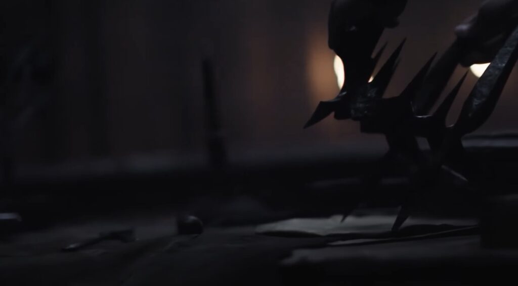 A dark, barely lit shot of Morgoth's crown being placed by a person out of shot on a table