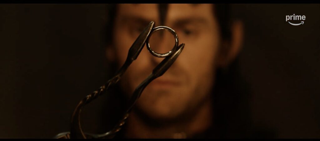 Out-of-focus Sauron holding the One Ring up on tweezers in front of him, in the centre of the shot in crisp focus
