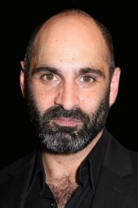 Promotional front-on headshot of Zubin Varla with a black background. He is a balding middle-aged man with trimmed full black beard