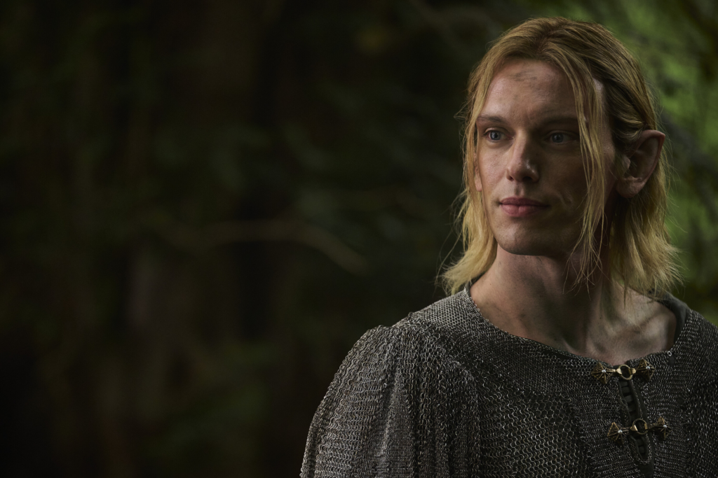 Jamie Campbell Bower as Celeborn, wearing chain mail, in a forest scene