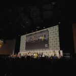 Photo of the 2024 San Diego Comic Con Rings of Power panel in Hall H, taken by Tea With Tolkien, showing the cast and showrunners arrayed on stage for the main panel