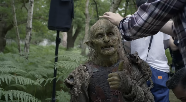 Behind the scenes picture of Adam Young in costume as Marnûkh having his wig adjusted while looking at the camera and giving a thumbs-up