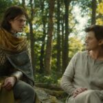 Elros wearing armour and Elrond wearing simple clothes having a discussion in a wood. Both are played by Robert Aramayo. Credits: Polygon