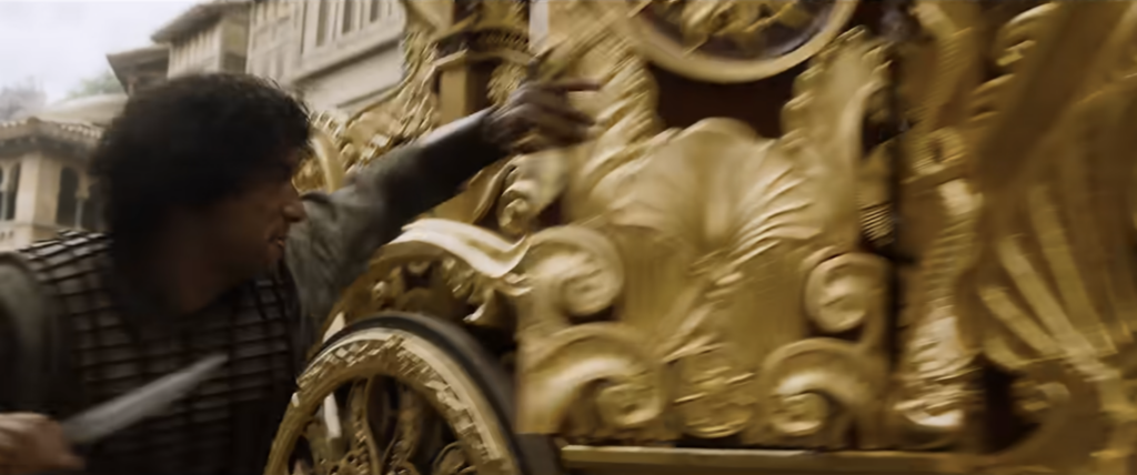 Blurry action shot of a man holding a knife pulling open the door on an ornate golden carriage