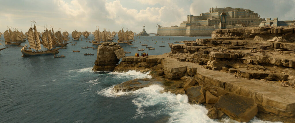 Large Númenórean fleet off a rocky coast with a large fortress city in the background