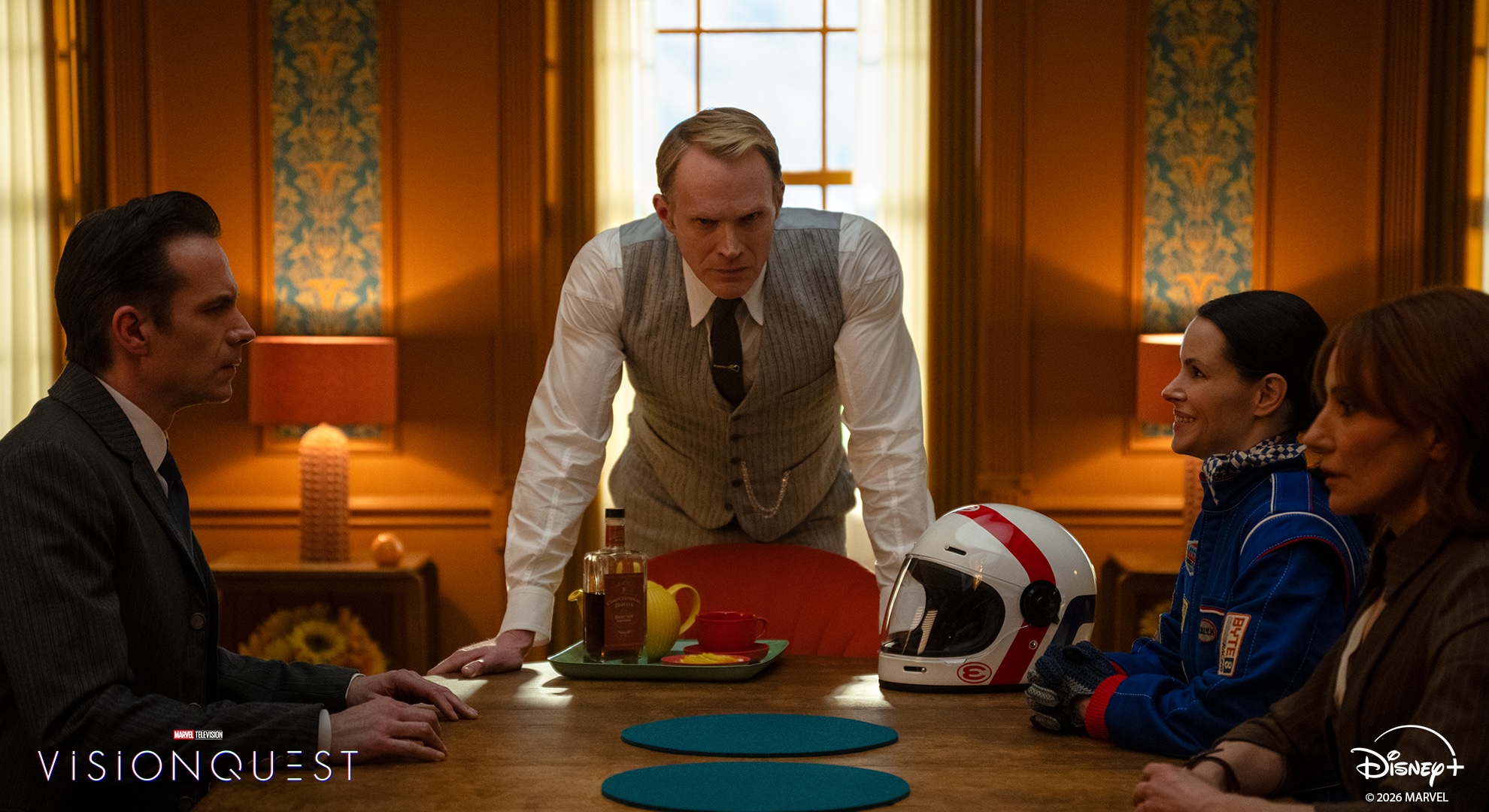 Vision standing at the head of a table, leaning forward on it with his hands, while human representatives in his mind palace flank him